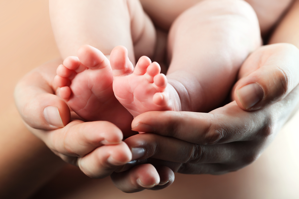 A newborn's feet encased between the hands of her mother